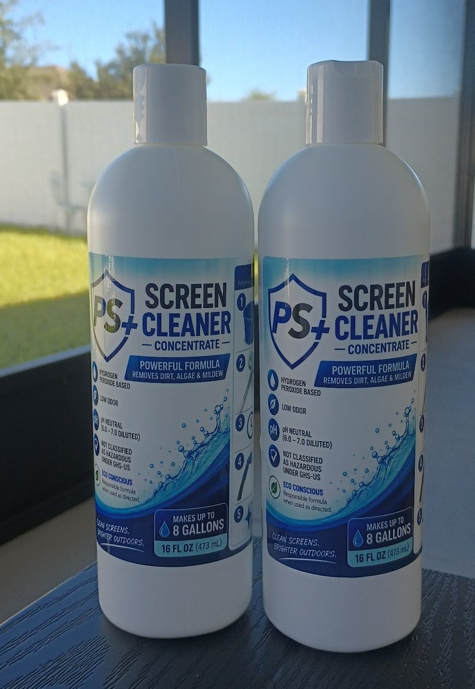 Two 16 oz bottles of PS+ Screen Cleaner Concentrate with white caps, standing on a table inside a screen enclosure